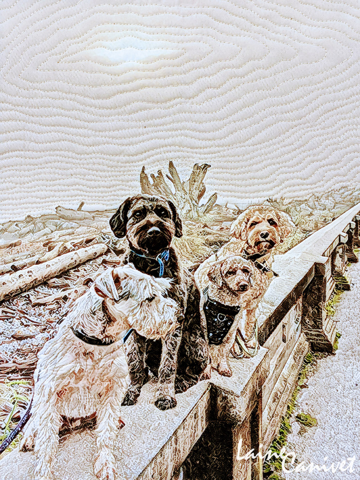 a quilt depicting four dogs sitting on driftwood at the beach