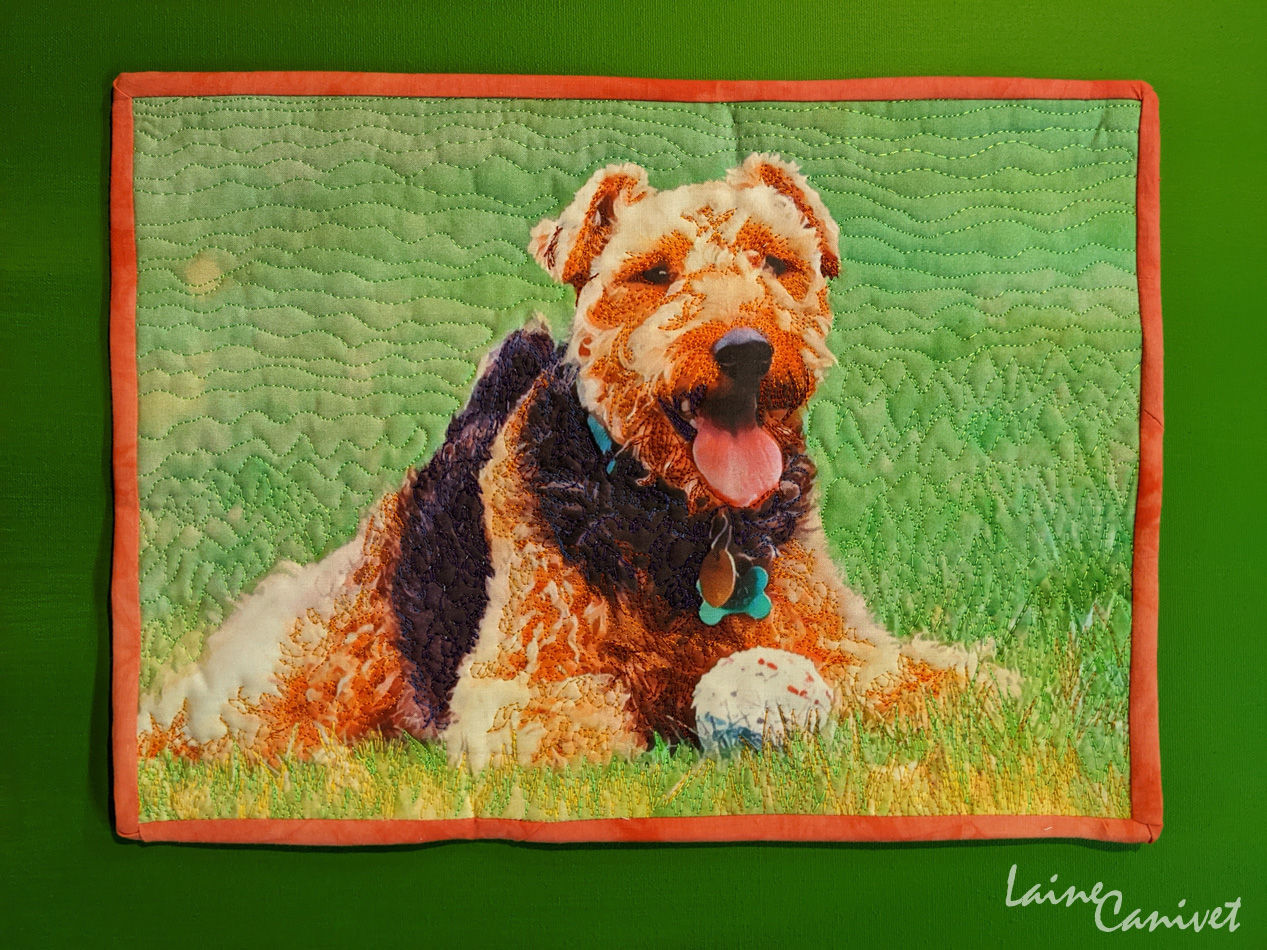 a fabric quilt depicting a brown and black dog on green grass