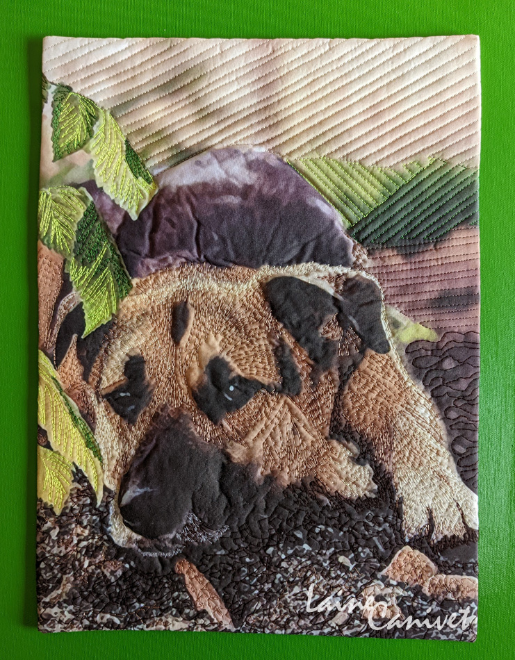 a quilt depicting a dog lying on the dirt behind some leaves